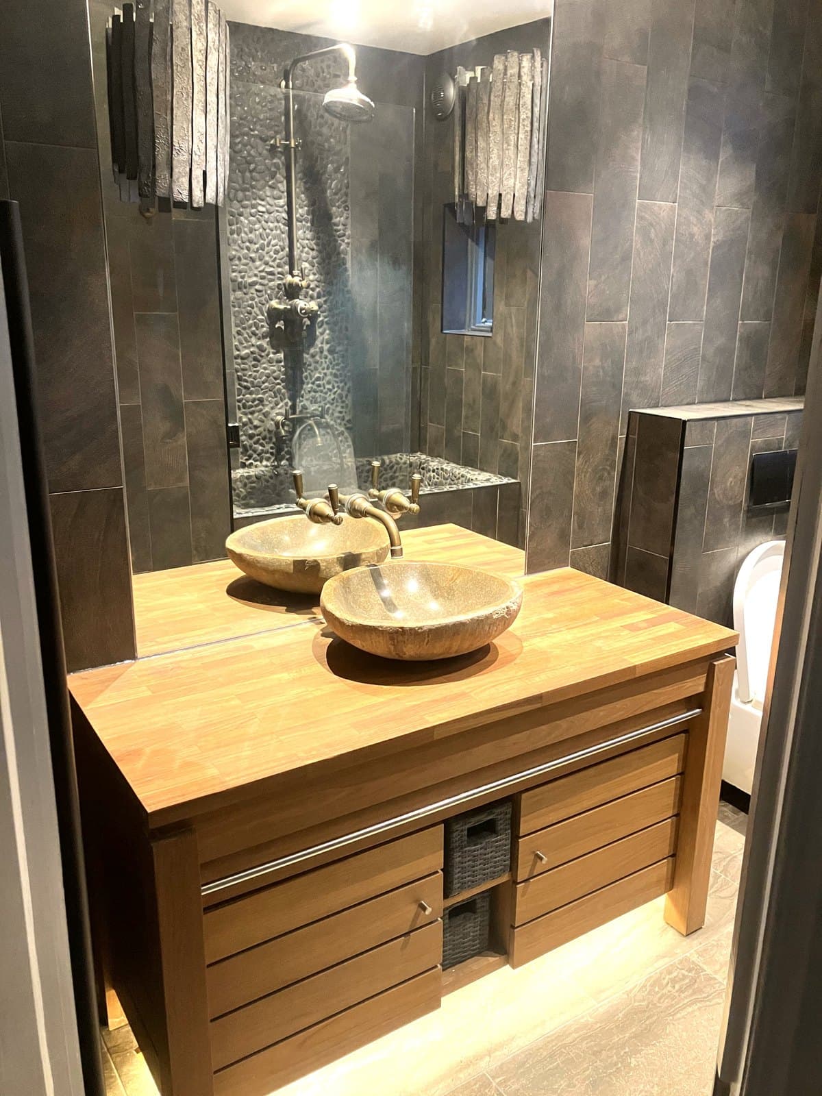 Spa-style bathroom with slate tiling, a pebble shower wall, oak vanity and stone vessel basins
