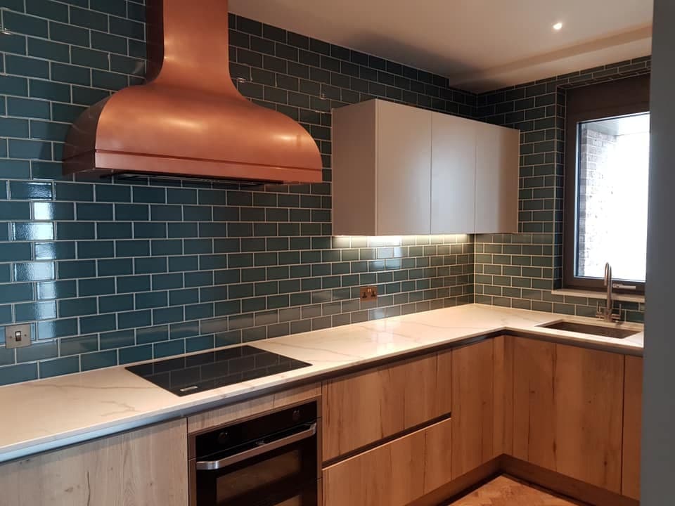 Kitchen with teal metro tiling, a copper extractor hood, oak cabinetry and stone worktops