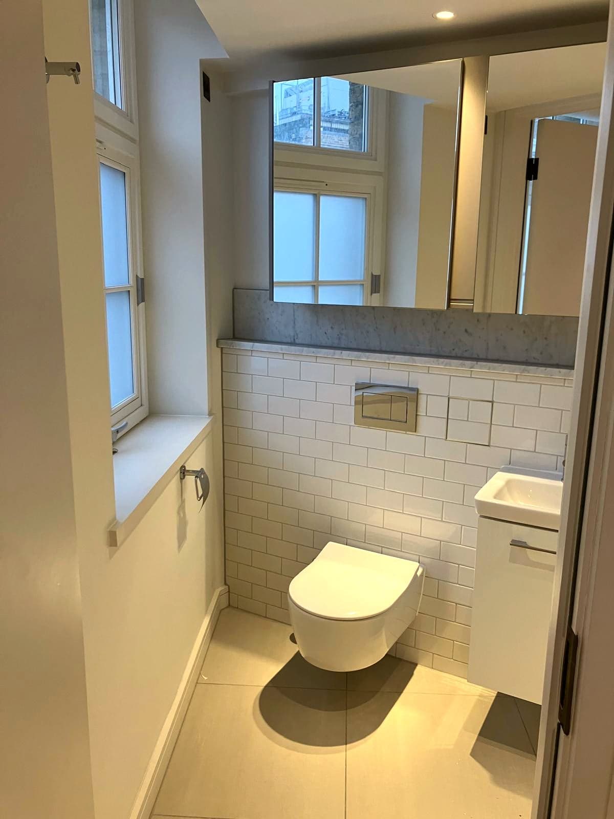 Wall-hung WC and vanity against white metro tiling beneath the sash window, Camden NW1