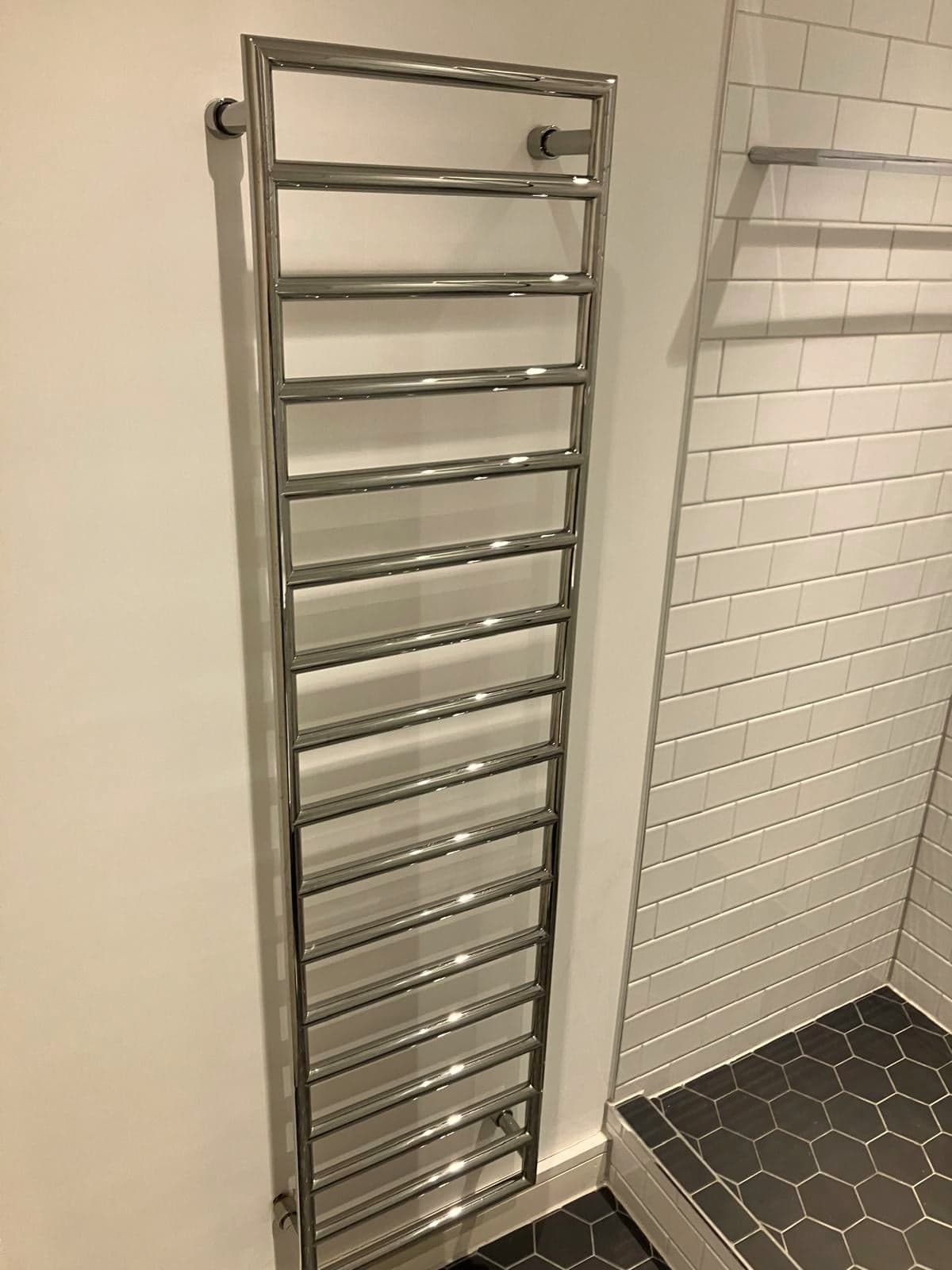 Chrome heated towel rail on the metro-tiled wall beside the shower tray, Marylebone W1