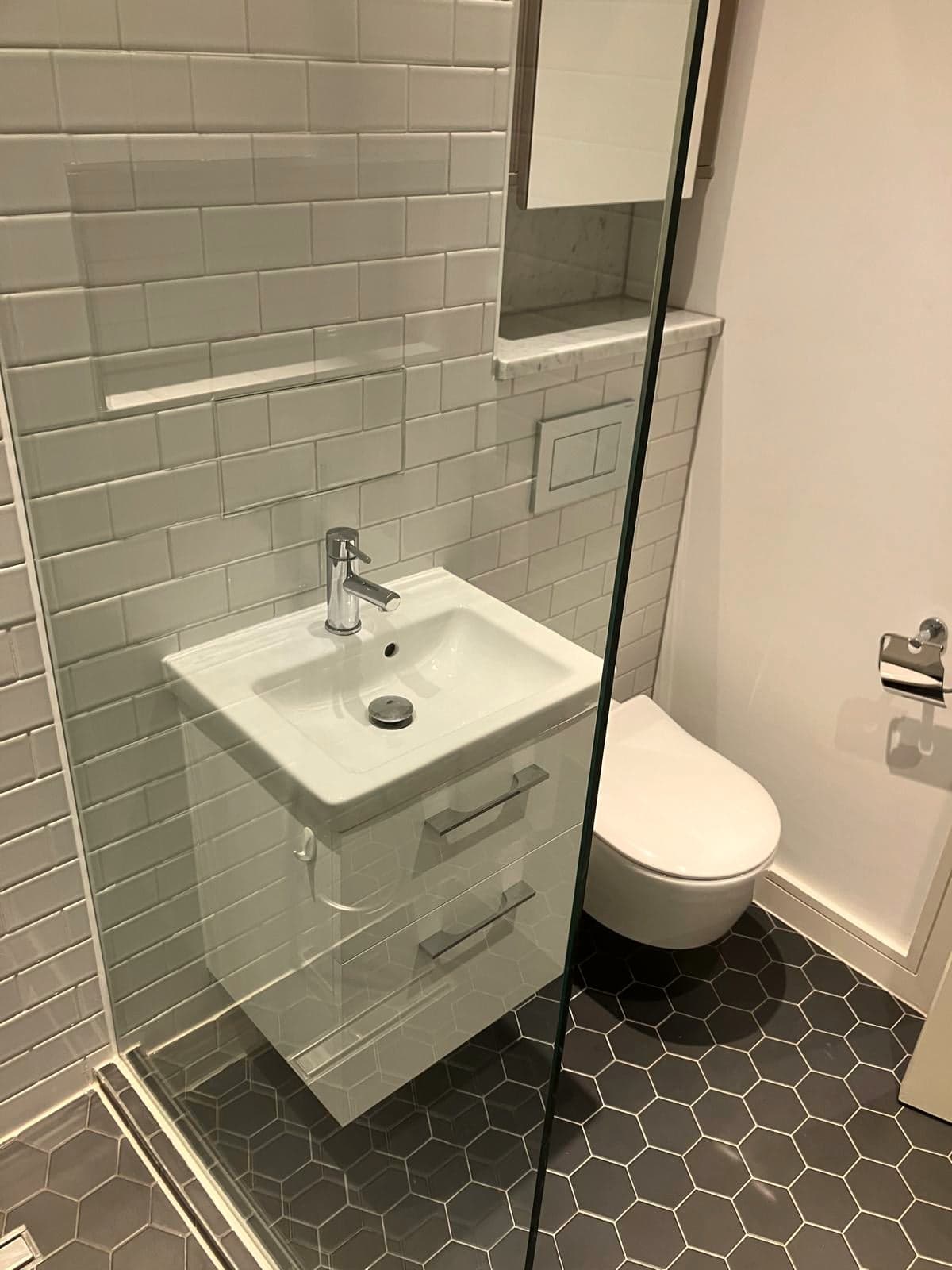 Wall-hung vanity, wall-hung toilet and hexagon floor tiles behind glass shower screen, Marylebone W1