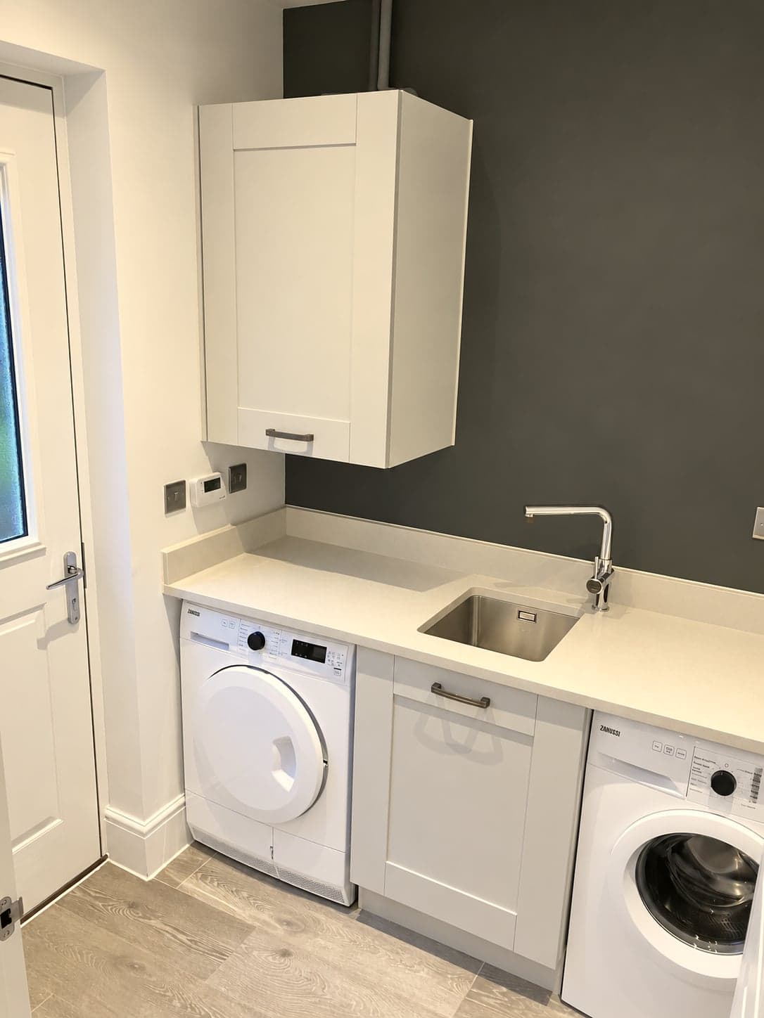 Utility room with sink, washing machine and dryer against a dark grey wall, Shepherds Bush W12