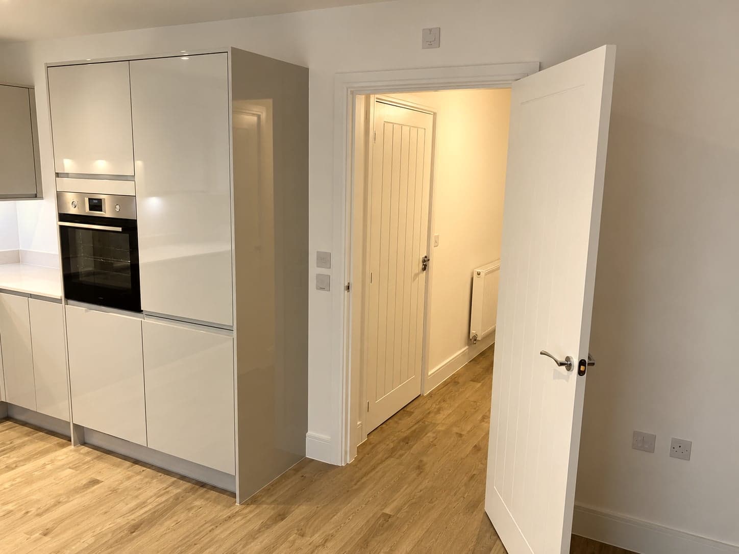 Oven housing and gloss units seen from the hall doorway, wood-effect flooring throughout, Hampstead NW3