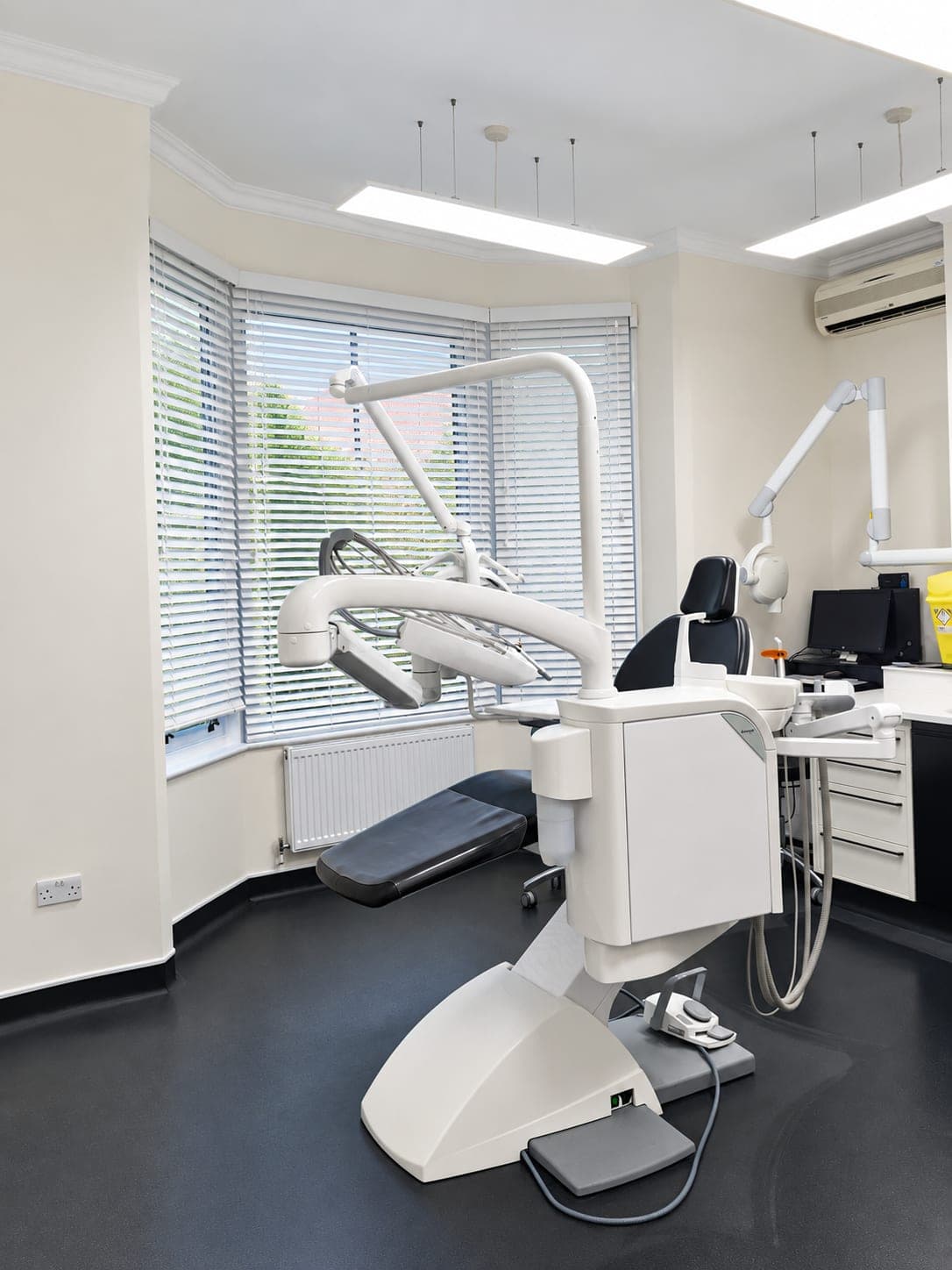 Dental surgery fit-out in a Victorian bay-window room with white and graphite cabinetry and dark safety vinyl, Haverhill CB9