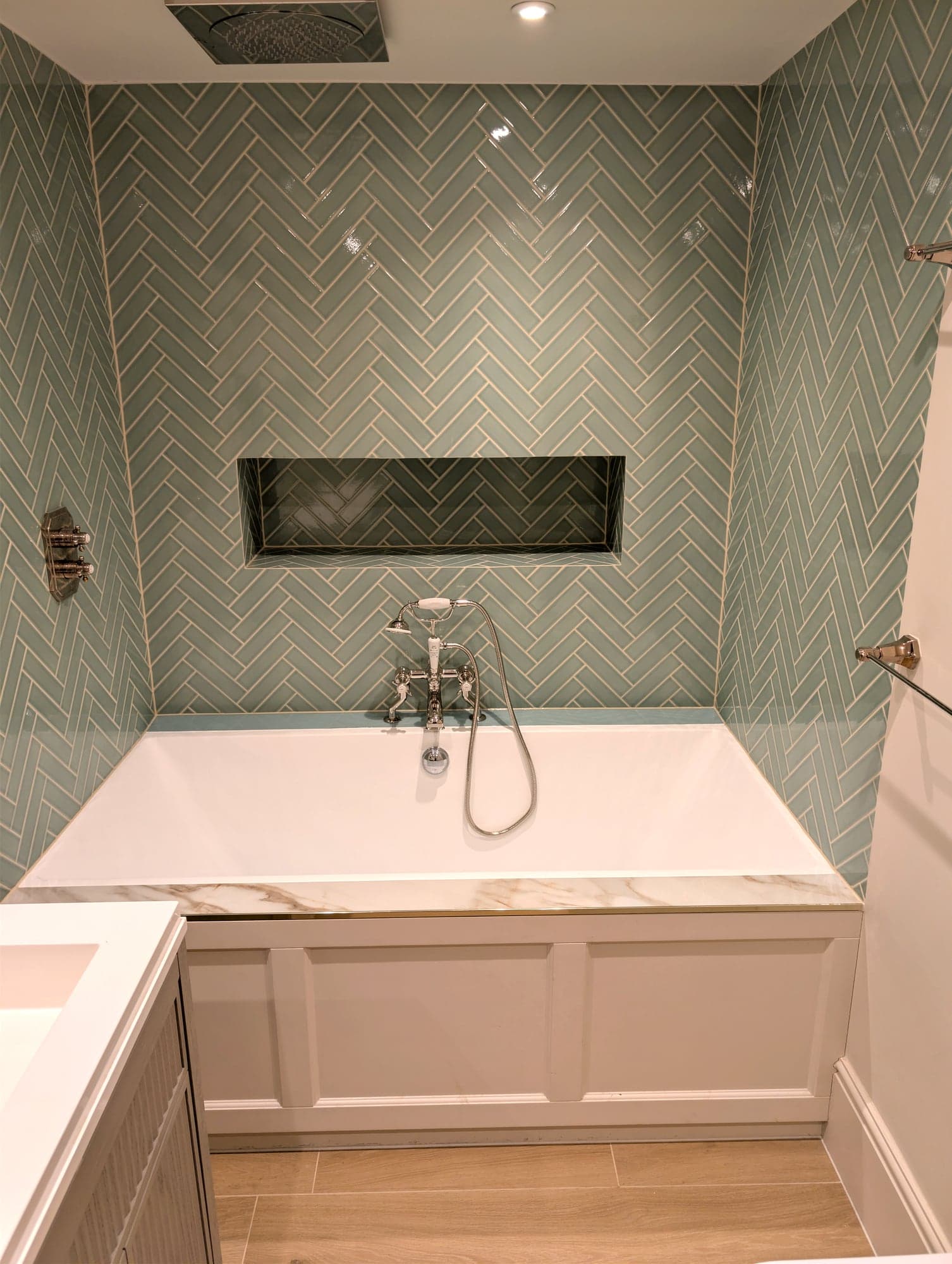 Sage herringbone tiled bath alcove with recessed niche, marble-topped panelled bath and nickel bath-shower mixer, Fulham SW6