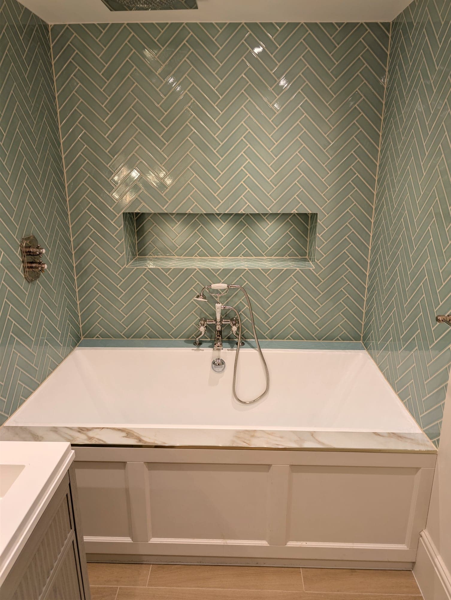 Marble-topped panelled bath against sage herringbone tiling with heated towel rail alongside, Fulham SW6