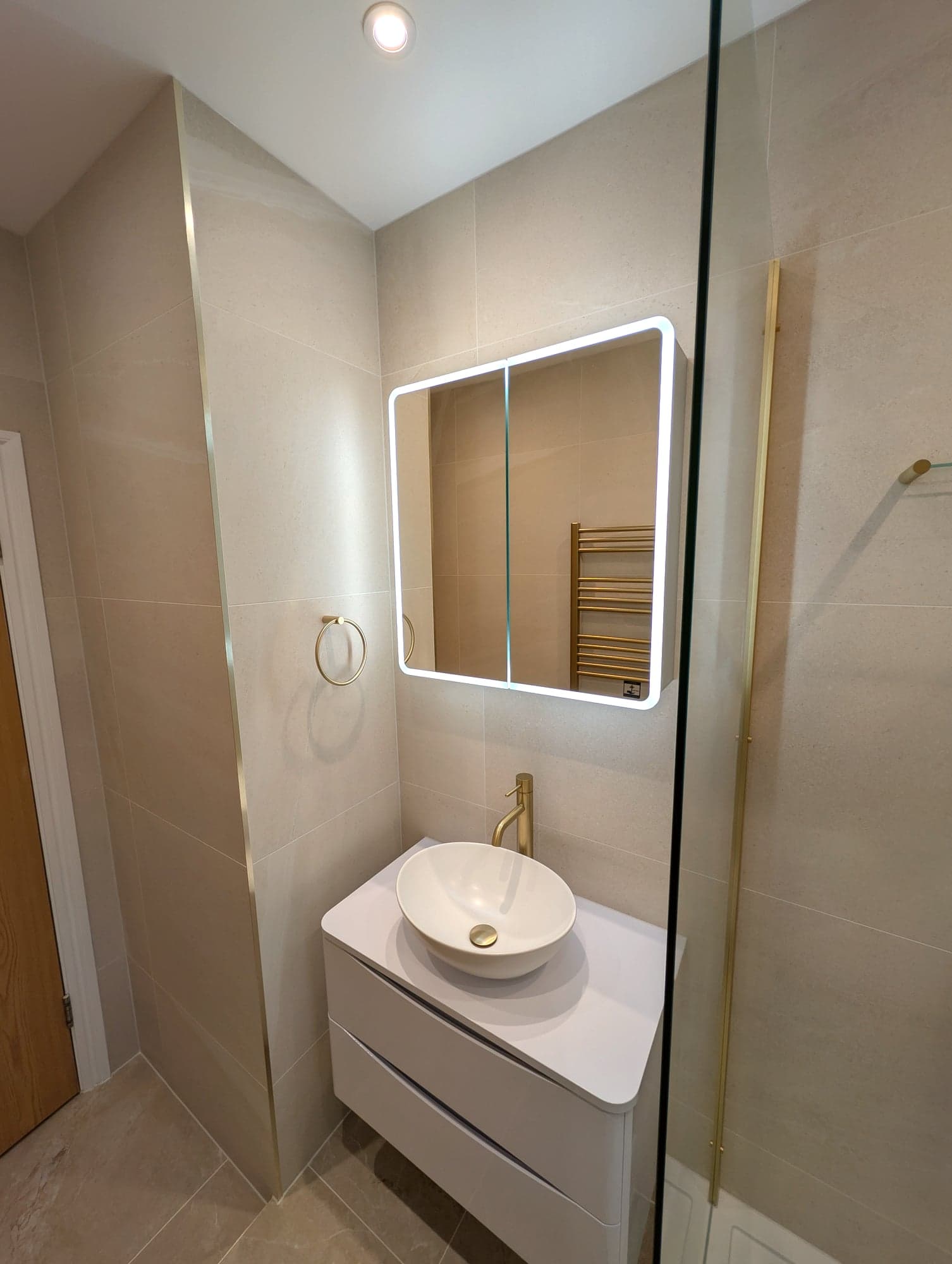Countertop basin, brass tap and backlit mirror against stone-effect tiling, Nine Elms SW8