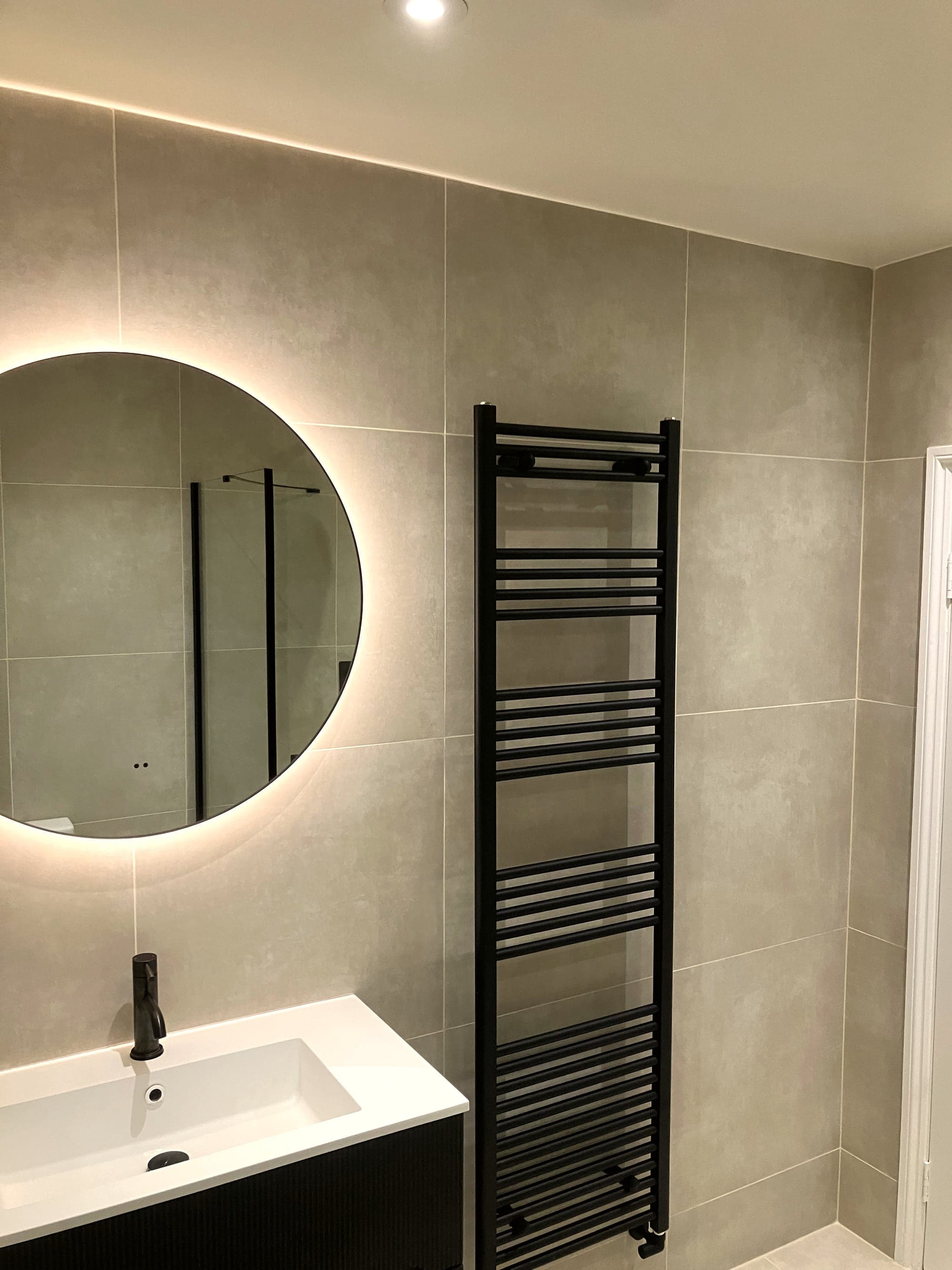 Backlit round mirror and black heated towel rail above the wall-hung basin, Clapham Common SW4
