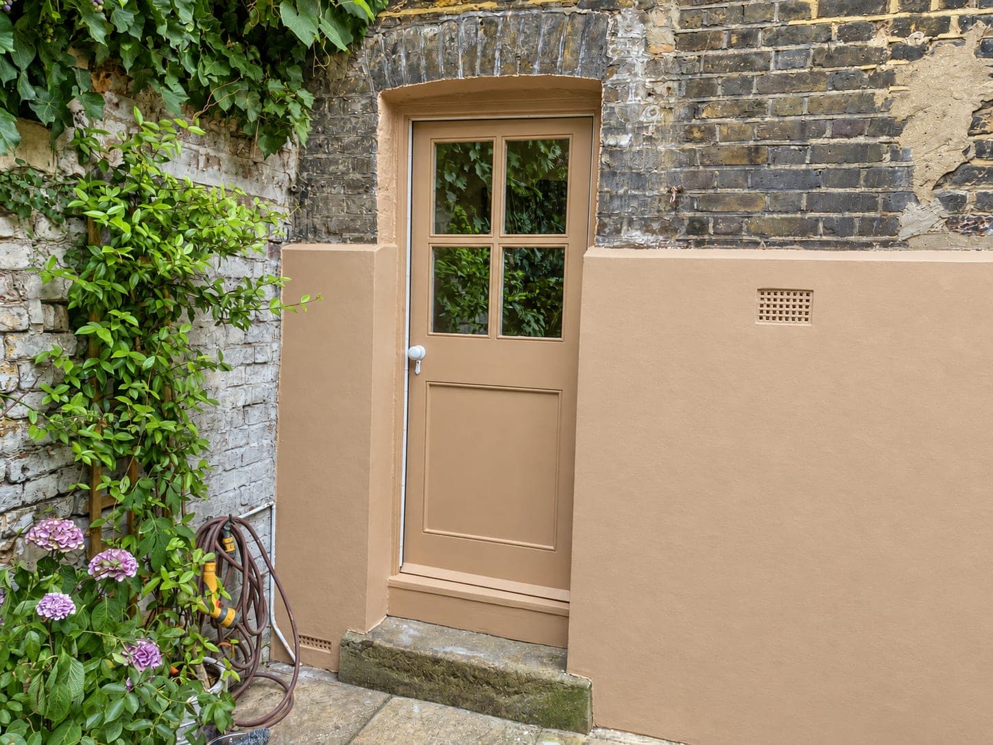 Rendered lightwell wall beside the painted timber door and planting, Hammersmith W6
