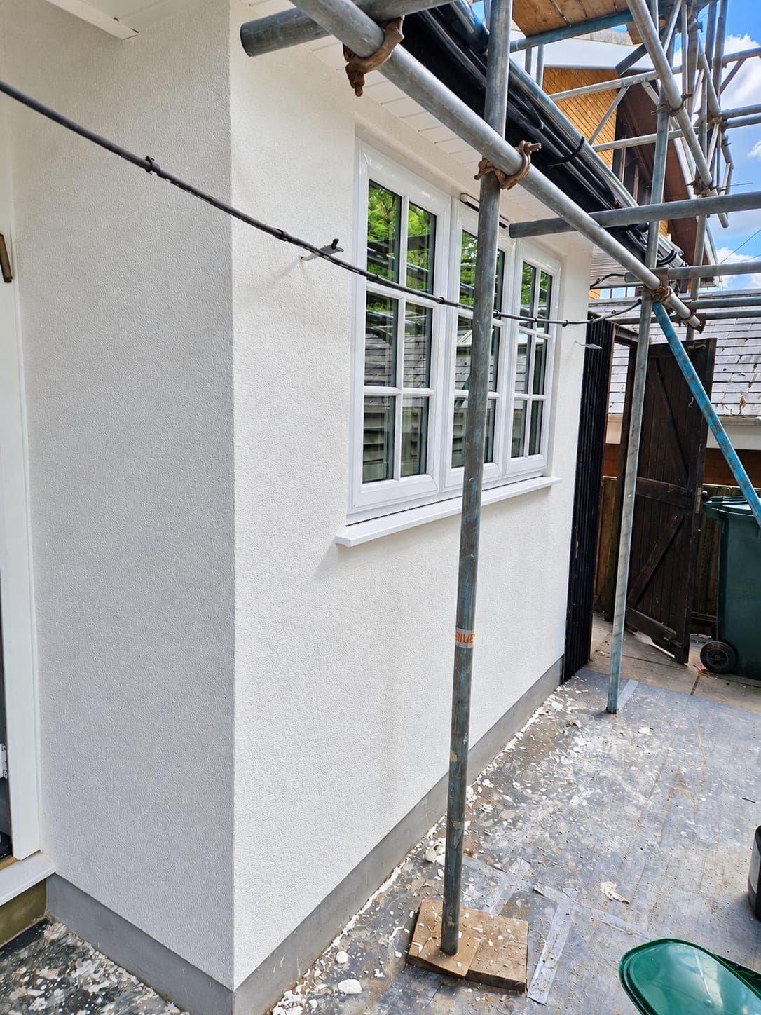 Detached house rendered in white with a dark plinth, bay window and black front door, Enfield EN3