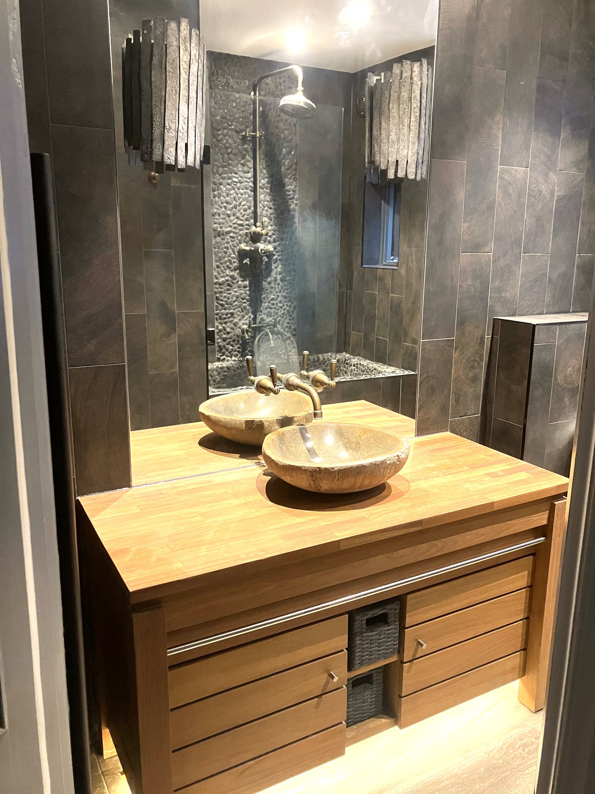 Oak vanity with stone basin and brass tap, mirrored to the pebble shower wall behind, Camden NW1