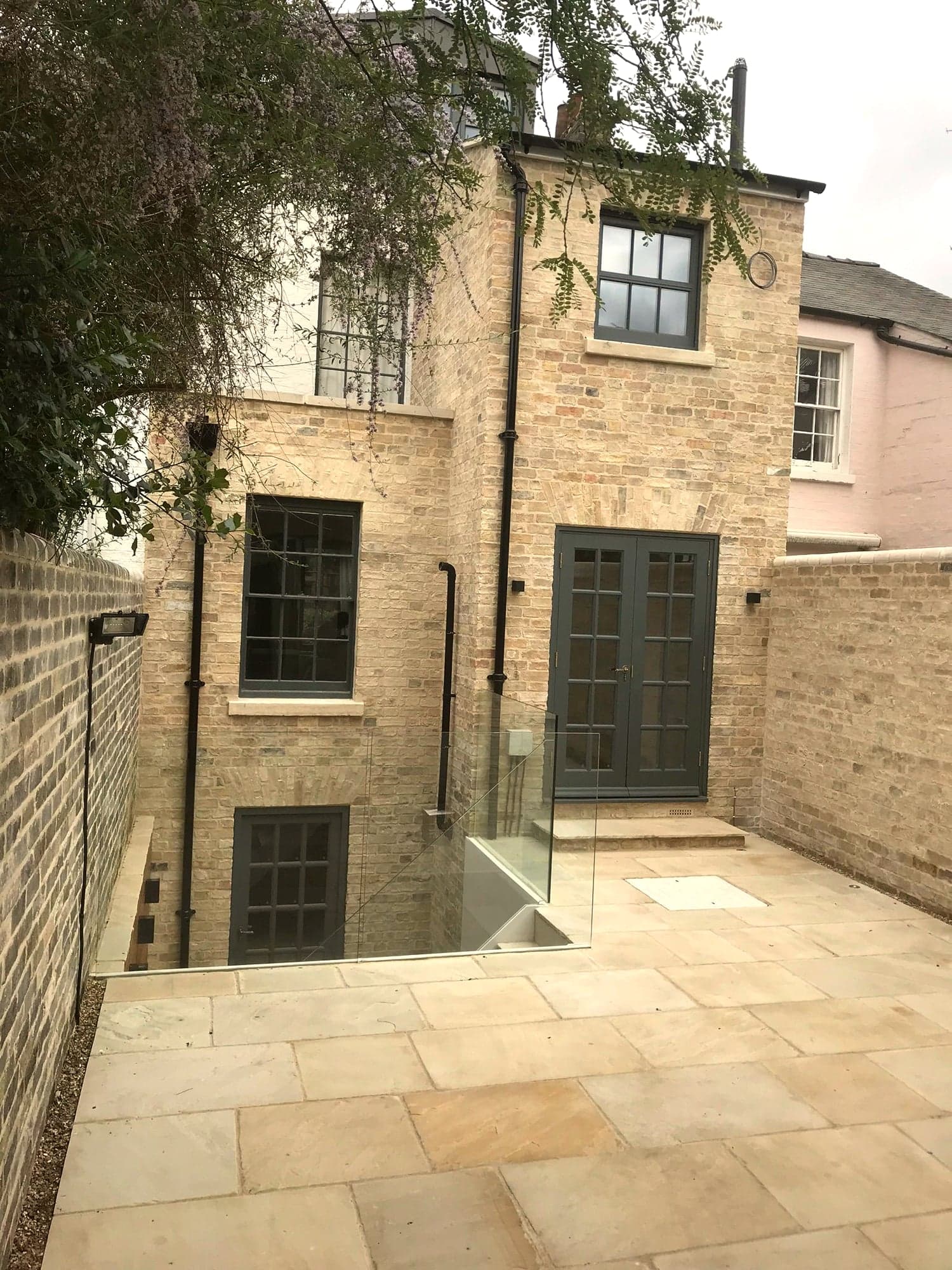 Stone extension and sunken courtyard seen across the paved garden, Kensington W8
