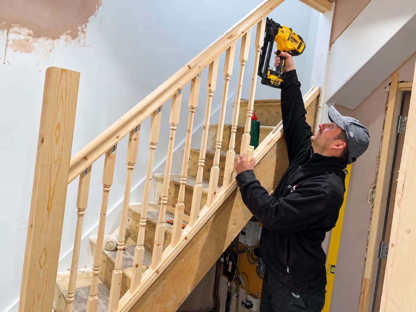 Carpenter fixing staircase spindles with a nail gun, London