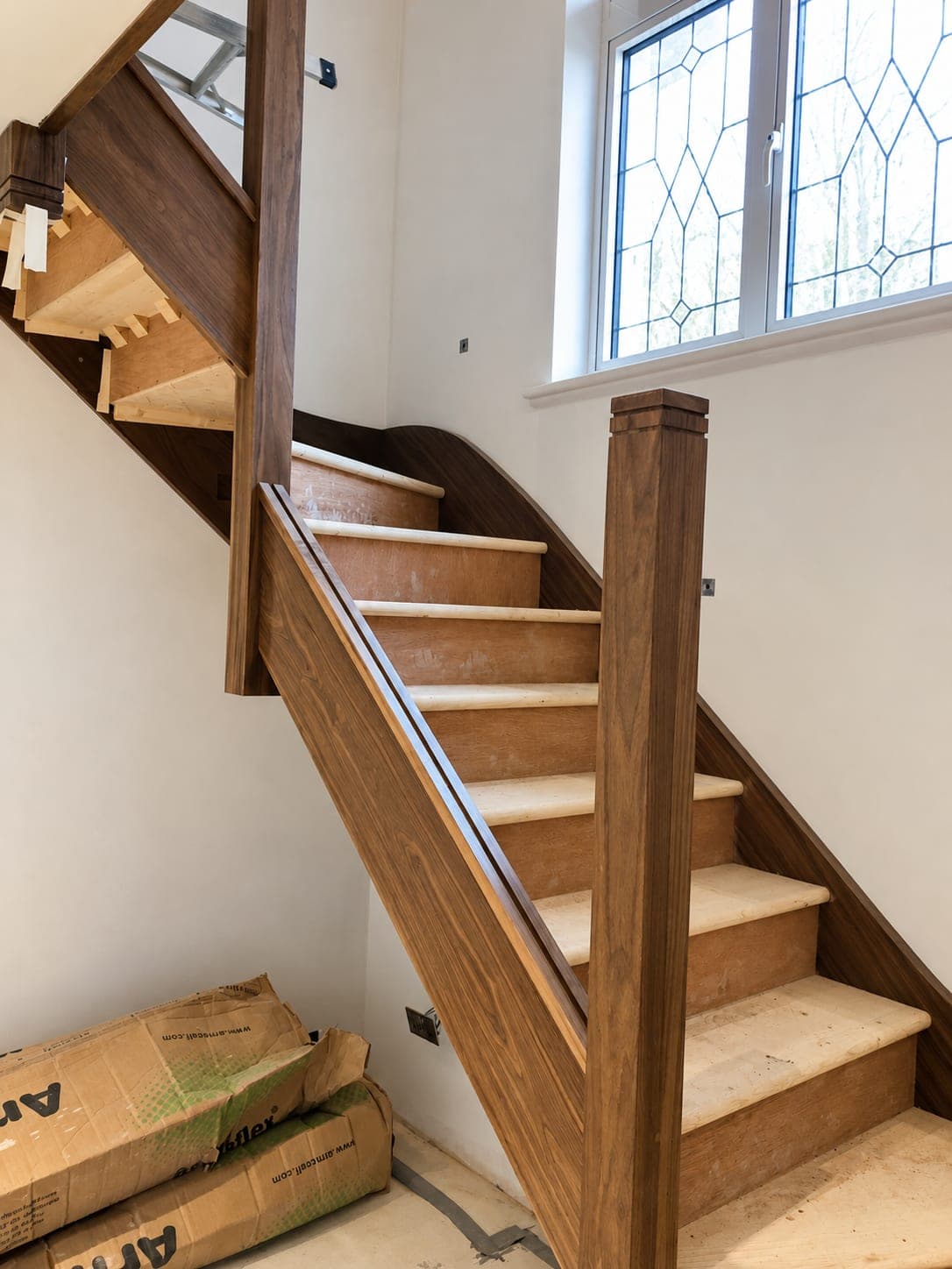 Oak handrail and newel post on a staircase beside a stained glass window, London