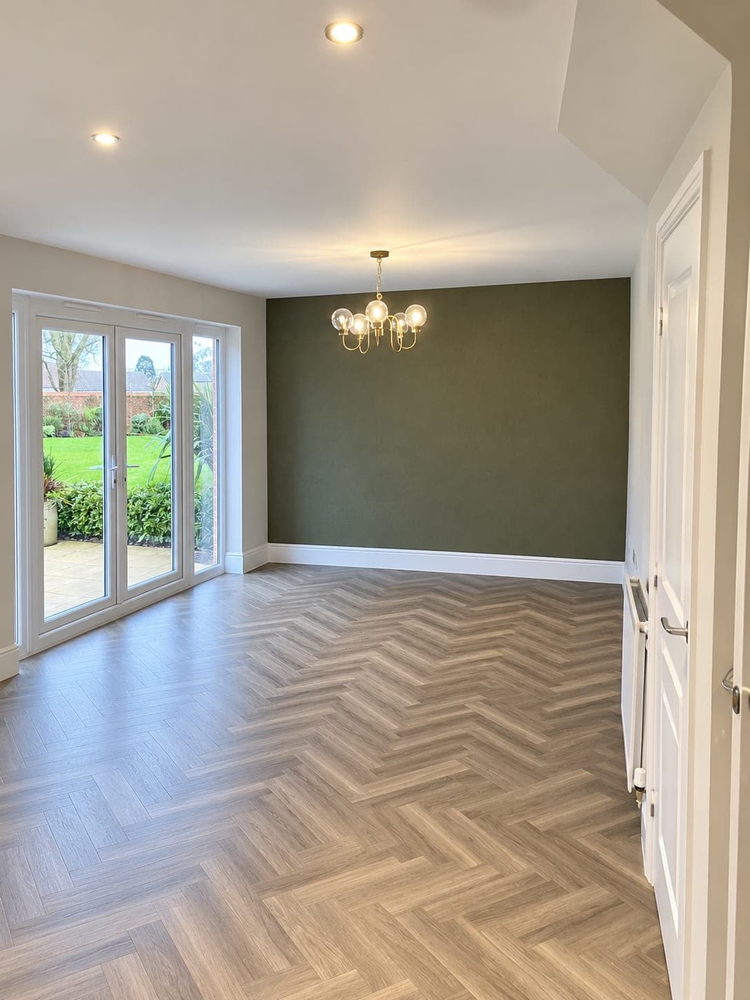 Herringbone wood flooring in a living room with an olive feature wall, London