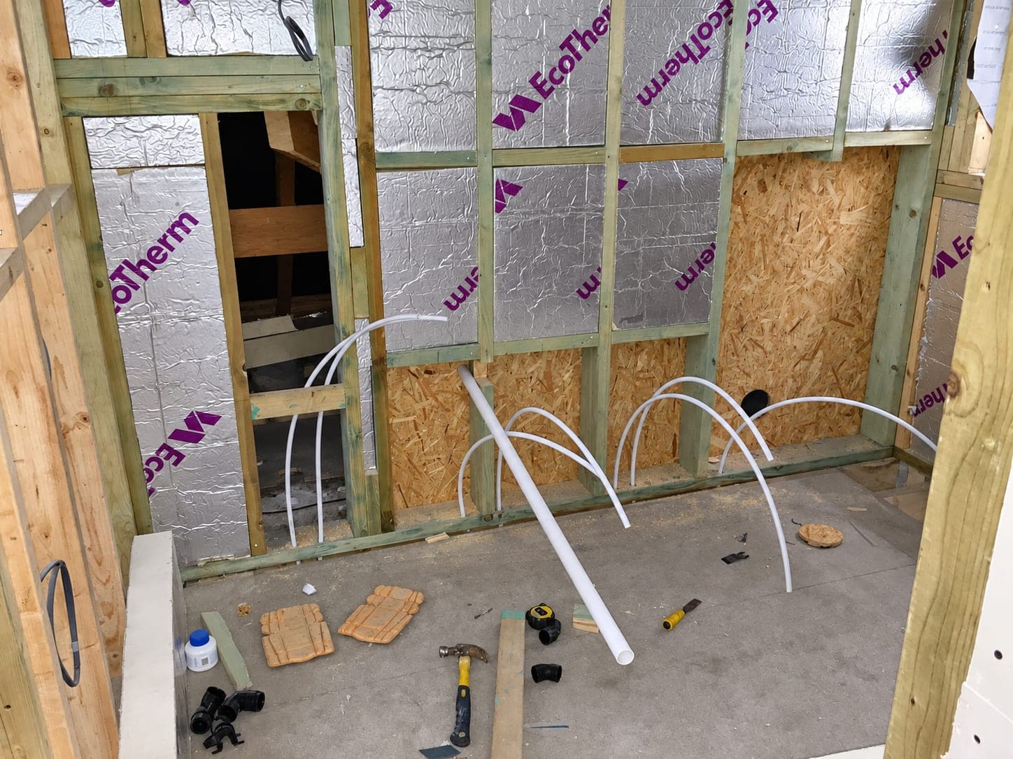 Pipe tails left through an insulated stud wall ready for second fix, London