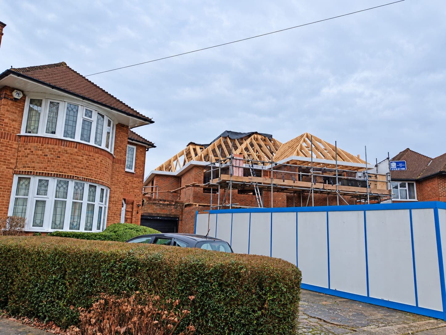 New roof structure going up behind site hoarding, seen from the street, London