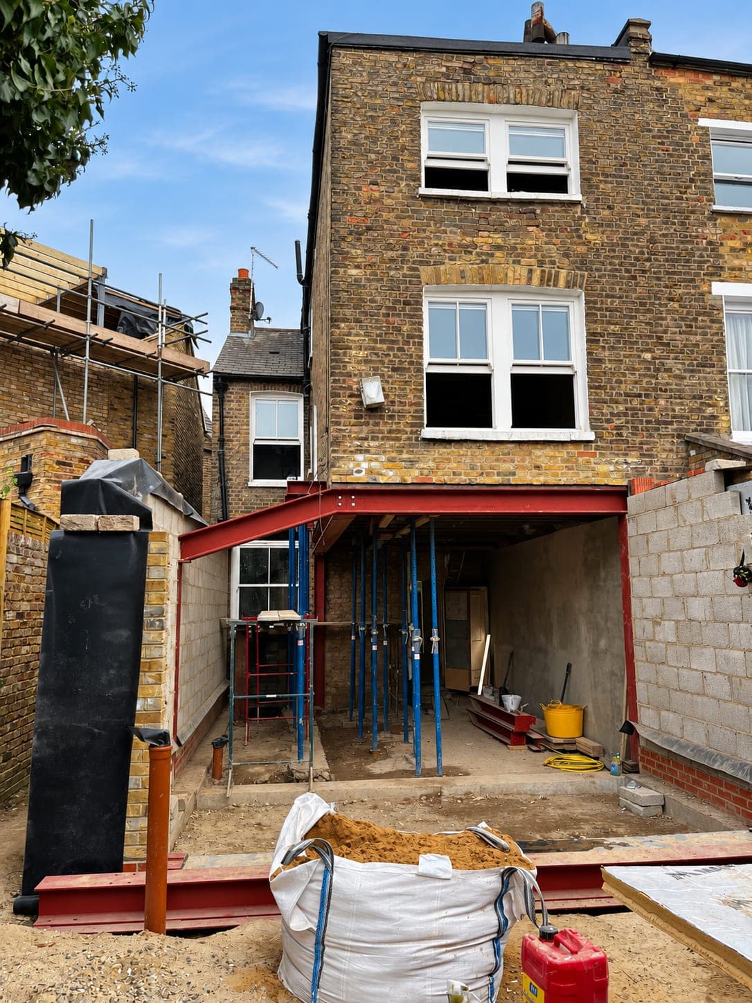 Steel goalpost frame installed across the rear of a house with Acrow props in place, London