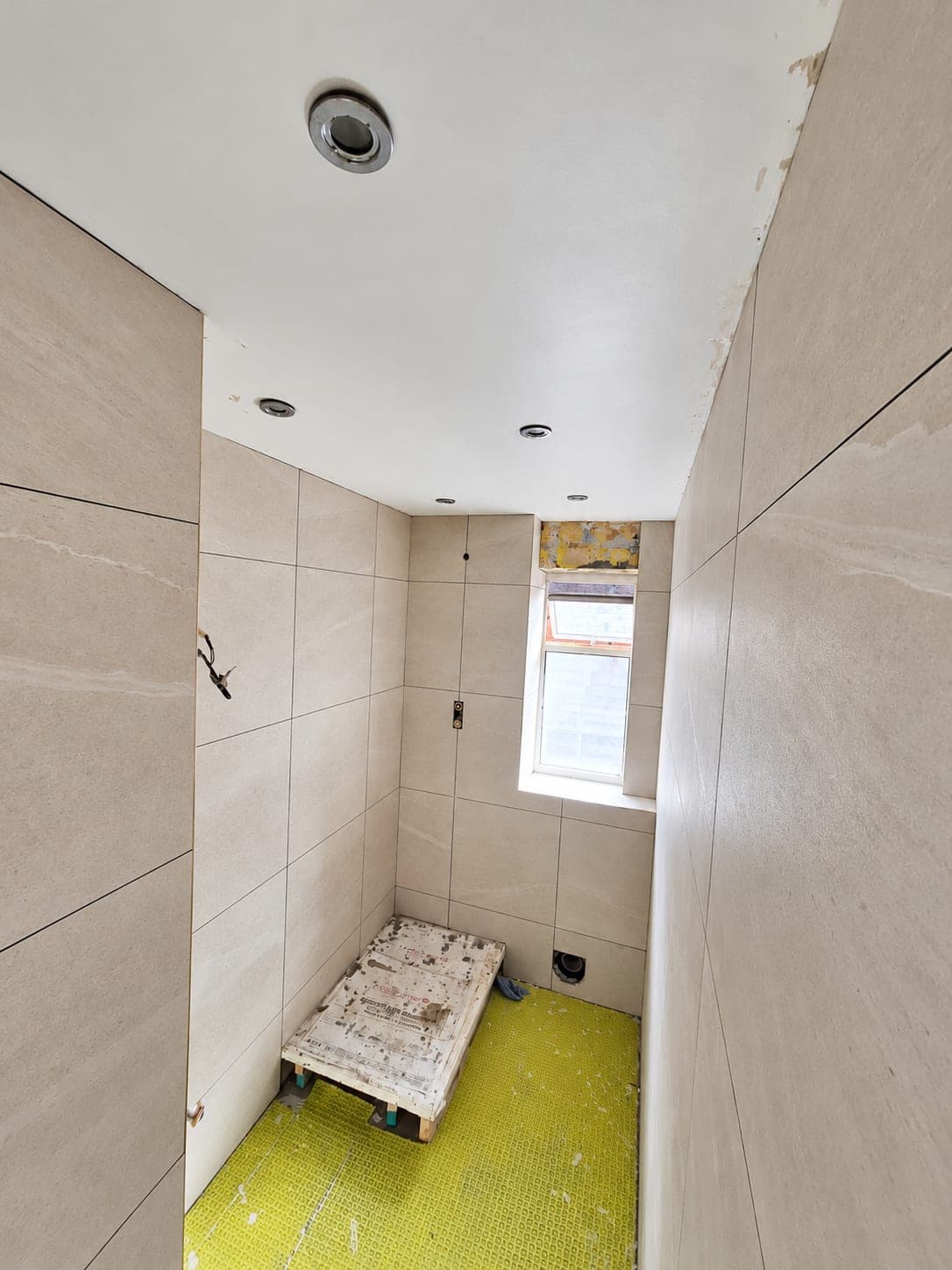 Full-height tiling to a bathroom wall with downlights above, London