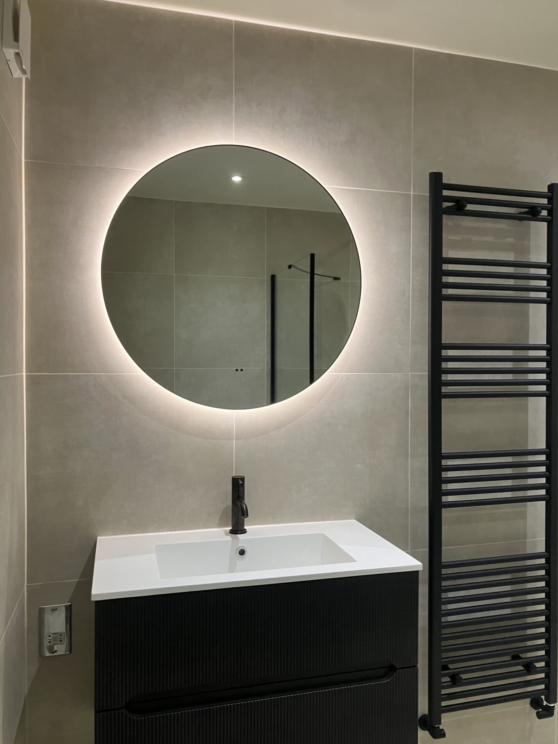 Vanity unit with backlit round mirror and black heated towel rail in a modern London bathroom